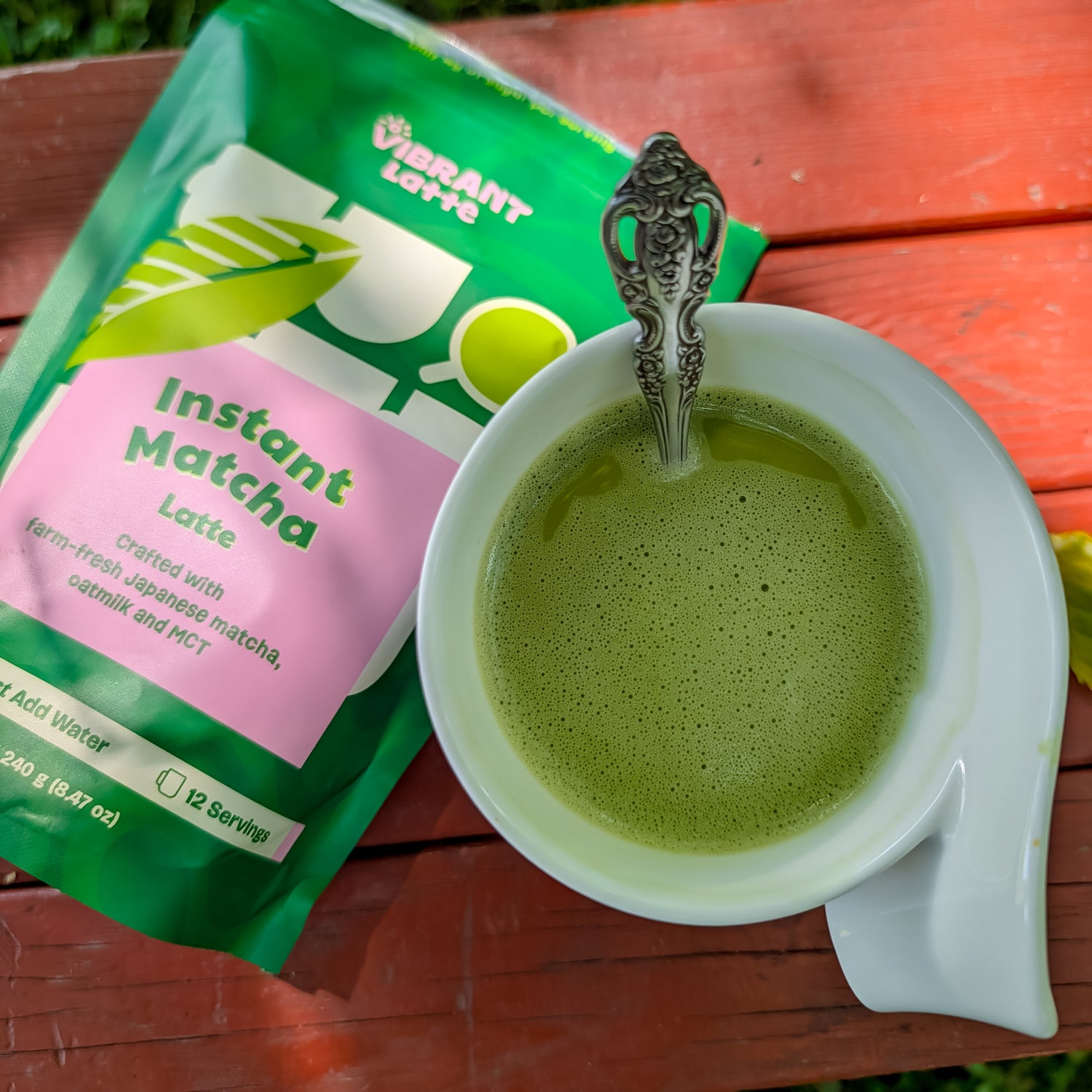 Green matcha latte in a white cup with a spoon, next to a Vibrant Latte instant matcha latte package on a wooden surface