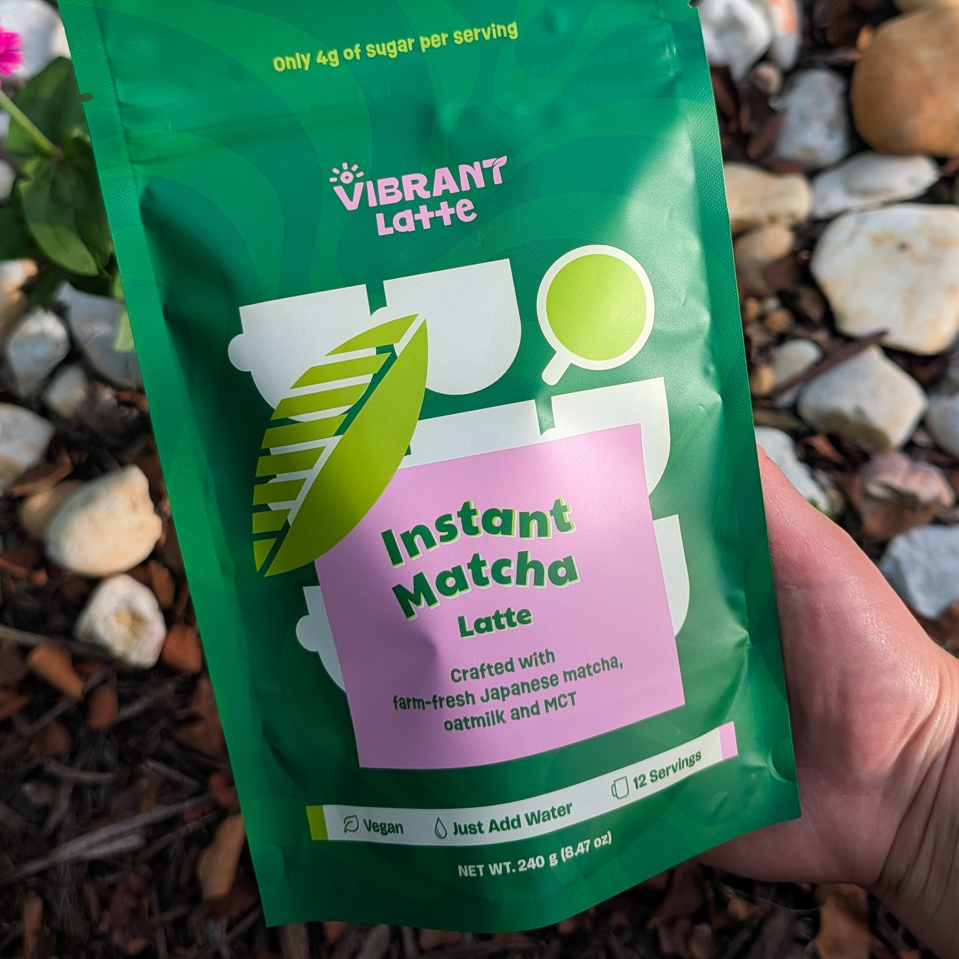 Green package of Vibrant Latte Instant Matcha Latte held over a natural background with stones and plants.