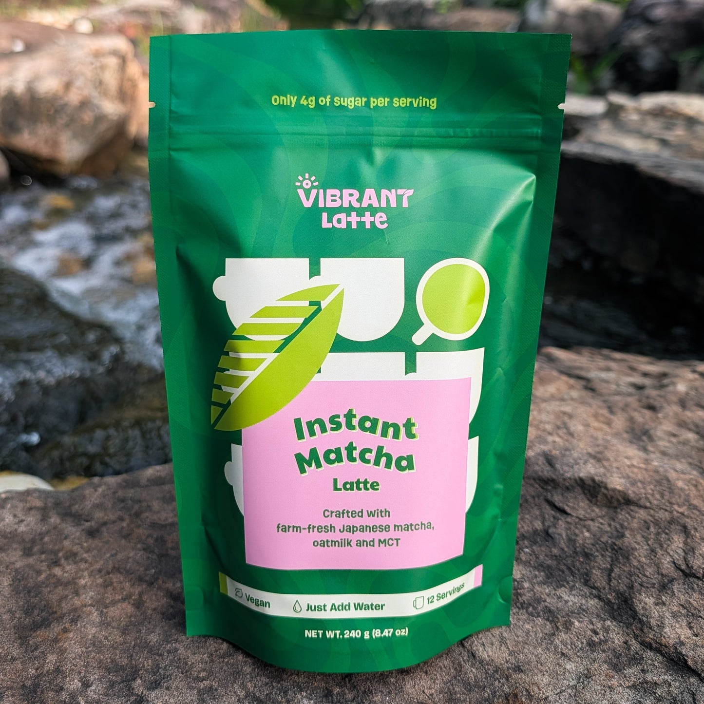 Green package of Vibrant Latte Instant Matcha Latte on a rocky surface with a natural background