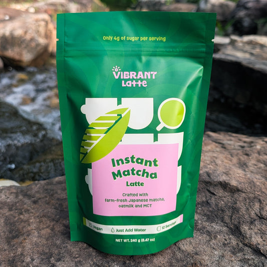 Green package of Vibrant Latte Instant Matcha Latte on a rocky surface with a natural background